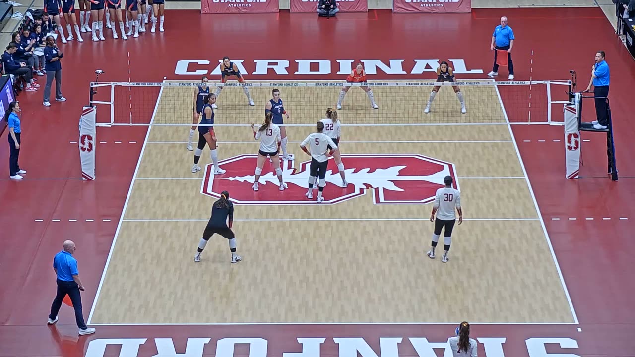 Stanford home match filmed from the camera platform high behind the end line: the whole court on the red floor, net across the middle, both antennas, far end line clear.